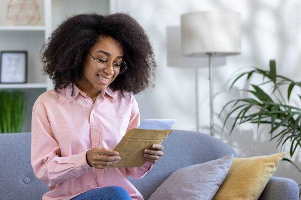 istock Woman reading letter at home on a cozy couch 2162513352