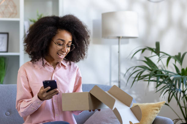 istock Woman excitedly opening package while using phone at home 2162513356