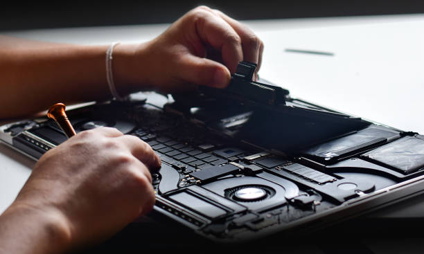 istock computer technician Laptop motherboard repairman using hands and screwdriver to remove or plug connector flex cable on computer motherboard. 2162514785