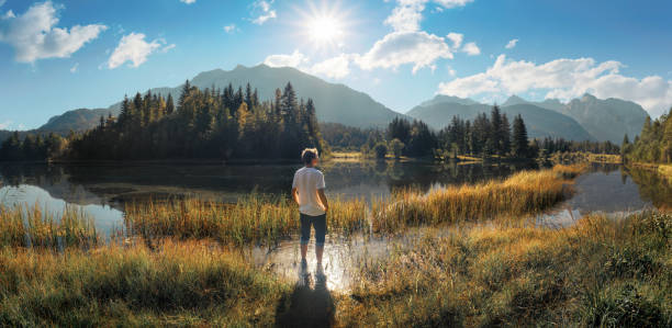 Painterly panoramic landscape with a man standing in the shallow water on a lakeshore and enjoying the majestic sunny view