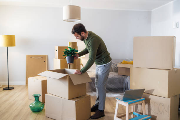 istock Man unpacking in new home surrounded by moving boxes 2162521189
