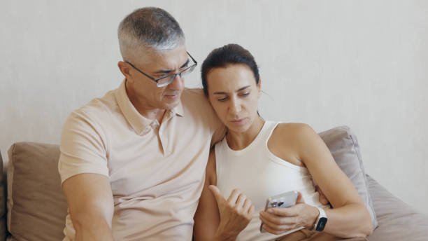 istock Couple Sitting on Sofa with Smartphone 2162522324