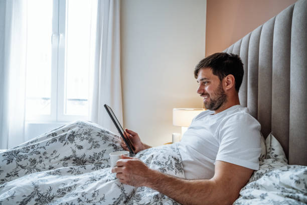 istock Single young man waking up in cozy bed and using digital tablet for work 2162548347