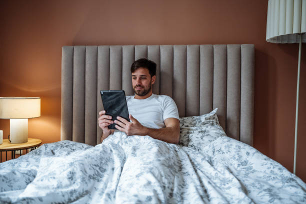 istock Serious young man waking up in cozy bed and using digital tablet for work 2162548368