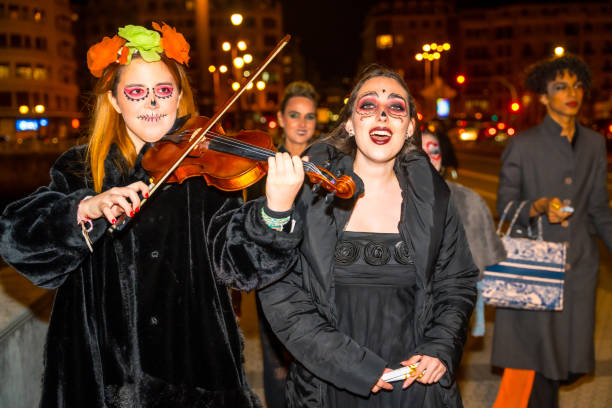 Two women dressed in Halloween costumes are playing violins