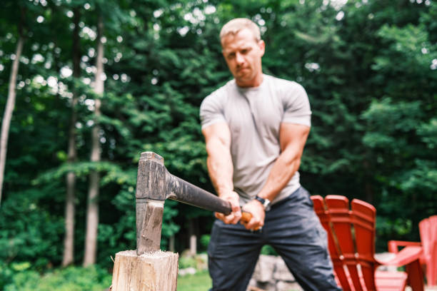 Young man chopping wood with axe. He is dressed in casual clothes. Exterior of vacation cottage in Muskoka, Ontario in Canada.