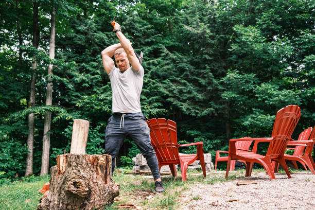 Young man chopping wood with axe. He is dressed in casual clothes. Exterior of vacation cottage in Muskoka, Ontario in Canada.