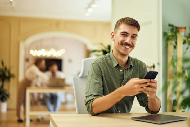 istock A smiling freelance man posing for the camera, working at the co-working space, using a mobile phone. 2162560400