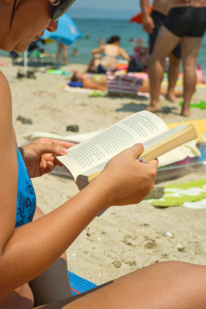 Young woman reading a book sitting on the bench on the beach at sunset.