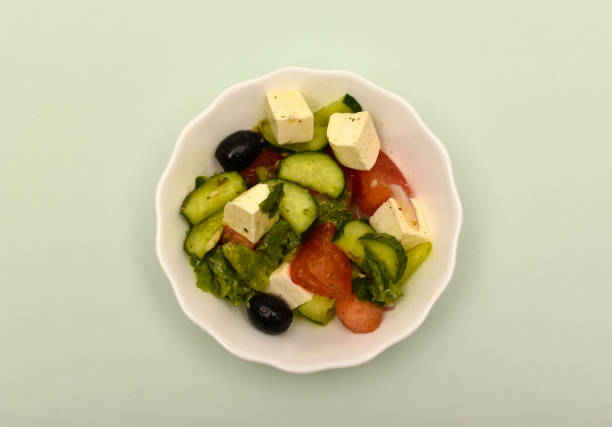 Greek salad in a white cup on a green background.