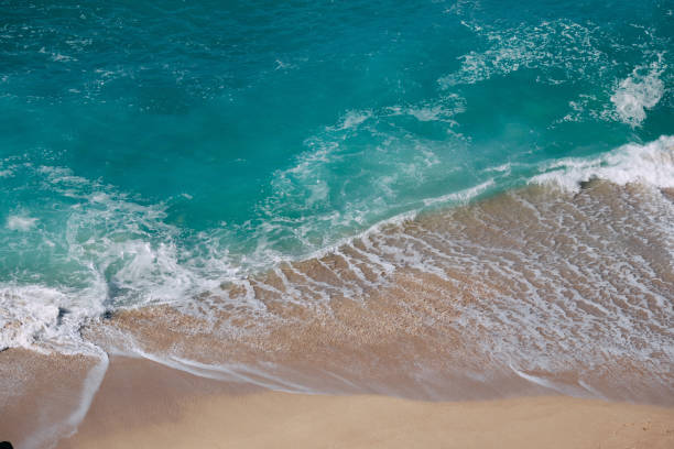 View down from cliffs onto breaking waves at Pedn Vounder Beach, near Porthcurno, Cornwall, on a sunny June morning.