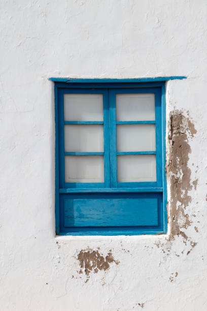 istock White weathered wall and a blue window, Spain 2162574173