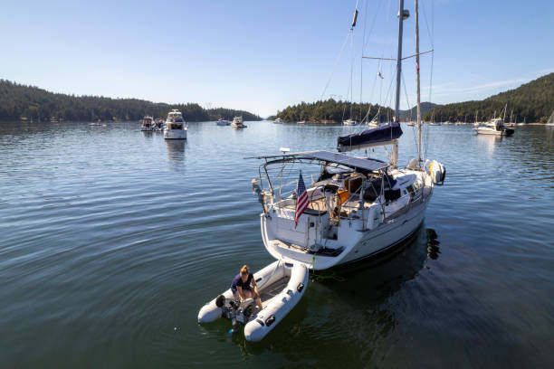 Woman prepares inflatable boat tied to sailboat in harbour, British Columbia