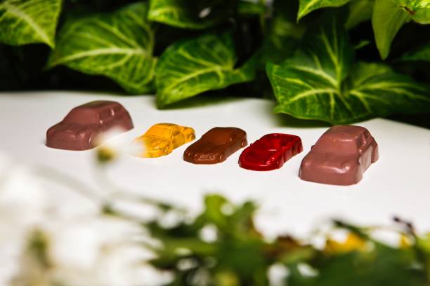 Five colorful gummy candies shaped like cars are arranged in a row on a white surface.