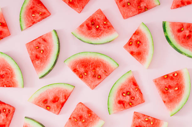 Trendy summer fruit pattern made with watermelon slices on light pastel pink background. Minimal summer concept. Creative food backdrop idea. Watermelon aesthetic.