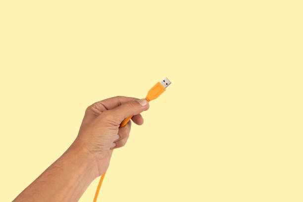 istock Male hand holding an orange usb cable isolated on light yellow background 2162585196