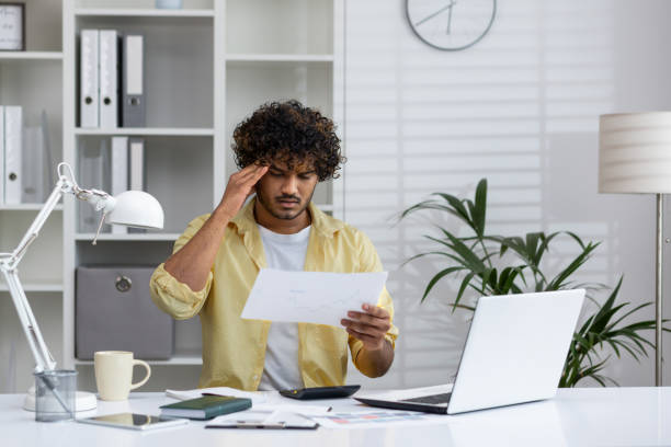 istock Stressed young man working at home with papers and laptop in modern home office 2162587957