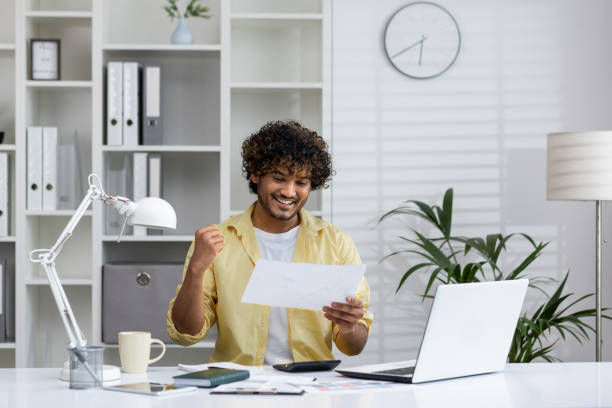 istock Happy businessman celebrating success with documents at modern office desk 2162589245