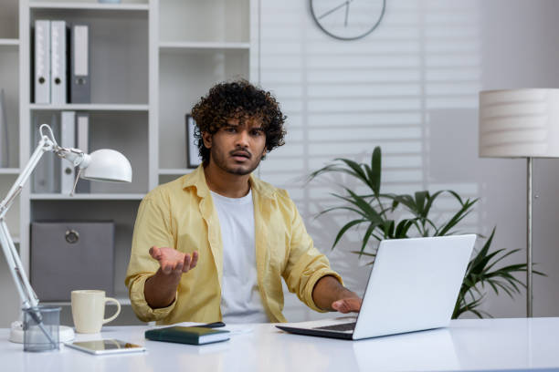 istock Confused man sitting in office with laptop, frustrated expression while working from home 2162589713