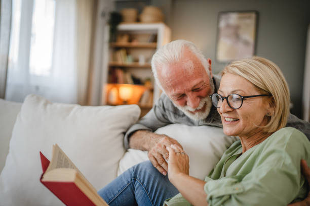 istock Mature wife lying down on sofa and read book whit her senior husband 2162590305