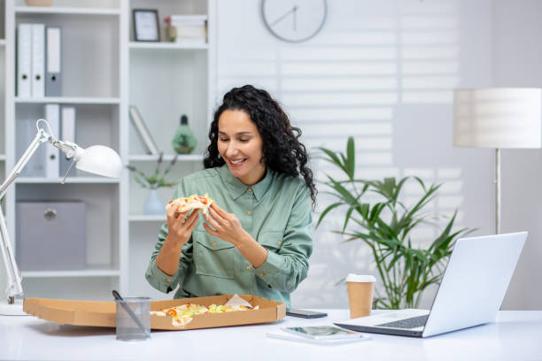 istock Hispanic woman enjoying a delicious pizza during work break in modern office 2162591968