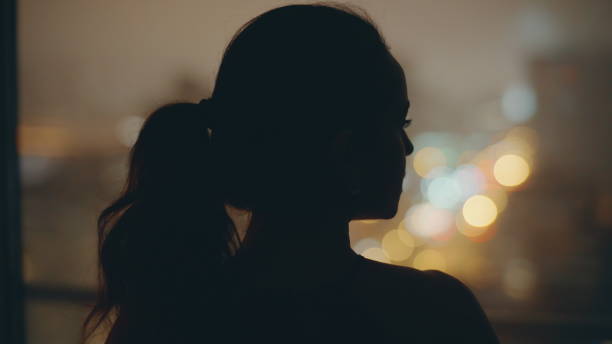 istock Night model looking panoramic window at dark flat back view. Woman thinking 2162592638