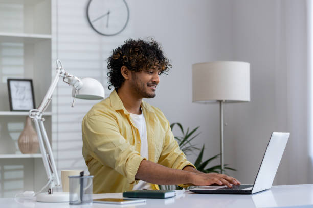 istock Smiling young man working on a laptop at home office desk 2162594415