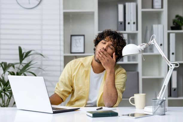 istock Tired man yawning at his desk while working on a laptop in a modern office 2162594979