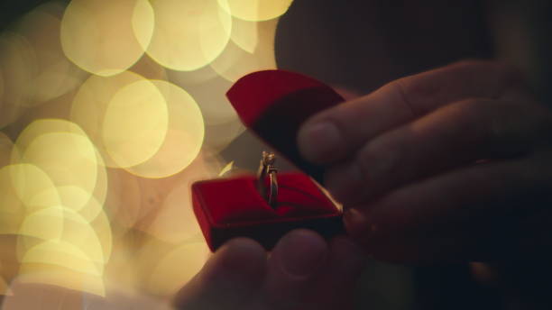 istock Groom hands opening ring red box at evening lights blurred background closeup 2162596119