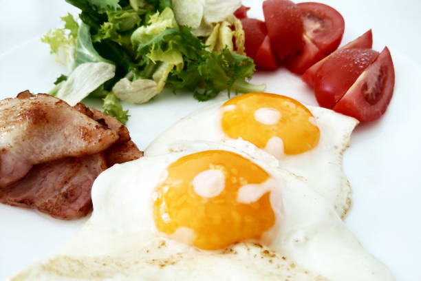 A beautifully plated breakfast featuring two sunny side up eggs, crispy bacon slices, fresh tomato wedges, and a green leafy salad. ideal for use in brunch menu design, healthy eating promotions, or nutritional presentations. the vibrant colors and appetizing composition make it perfect for food photography portfolios.