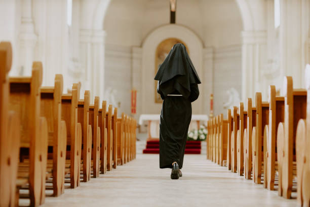 Rear view wide shot of unrecognizable Catholic nun walking along nave towards altar in church, copy space