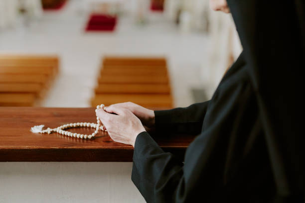 Medium closeup of hands of unrecognizable mature Catholic nun holding rosary beads in hands, copy space