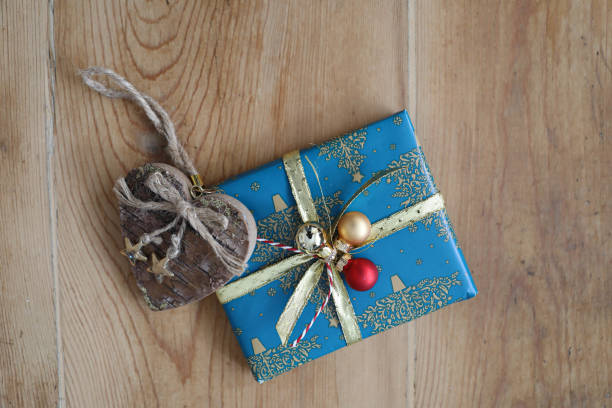 A beautifully wrapped gift with intricate wrapping paper and a decorative bow, placed on a wooden table, close-up. The focus is on the elegant presentation and details of the wrapping.