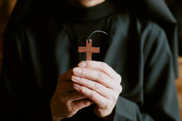 Cross In Nuns Hands Closeup shot of hands of unrecognizable mature Catholic nun wearing black habit holding wooden cross nun praying cross human hand stock pictures, royalty-free photos & images
