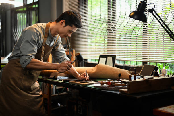 istock Male artisan holding a tool and a hammer to puncture or shape the leather on a workbench 2162632872