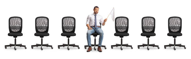 istock Sad businessman sitting between empty chairs and holding a white flag 2162638277