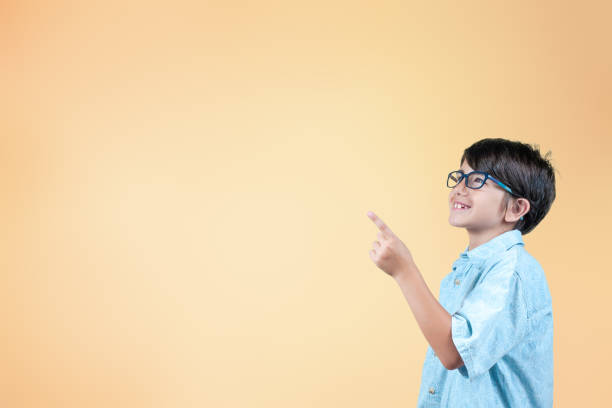 istock Smiling kid with glasses points to an empty marketing space on orange background. 2162644680