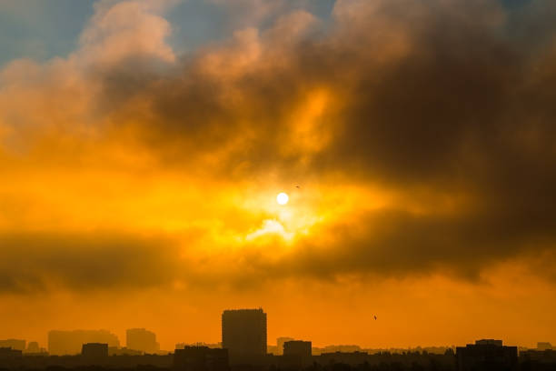 Dawn. Clouds cover the sun in the morning sky over the city. Birds in flight. Silhouettes of buildings in backlight