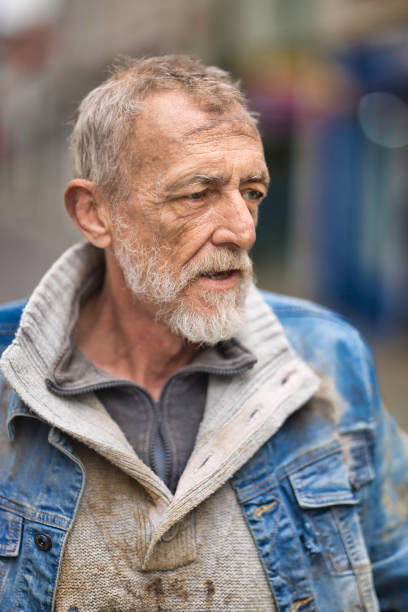Belgrade, Serbia - May 31, 2025: Homeless man sitting on grass in a city park with his head down and holding a cup. Symbolic image of poverty, struggle, and urban life challenges.
