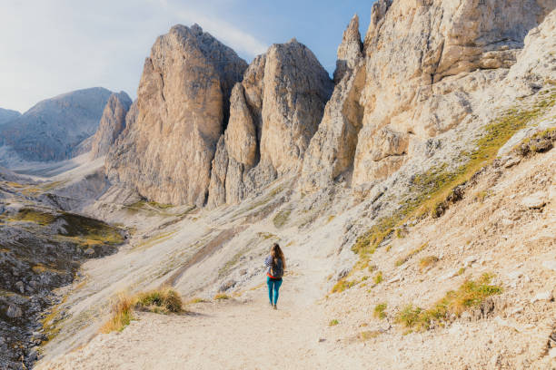 Rear view of woman with backpack admiring summer day outdoors in high attitude hiking in beautiful mountains through steep cliffs in Italy