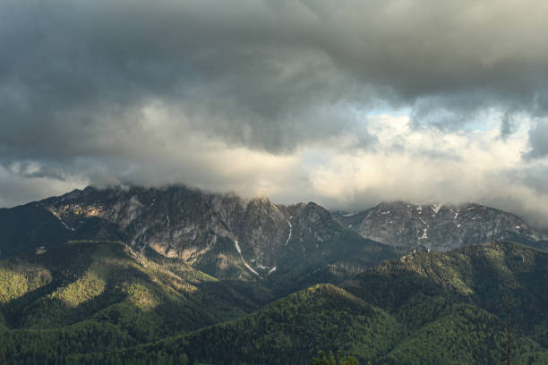 Tatra Mountains in Zakopane in spring, covered with cherished trees and remnants of snow from winter, big gray clouds enveloping the mountains