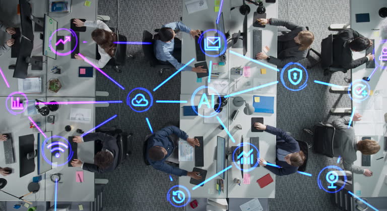 Top Down View of Employees Working in Office, Utilizing Artificial Intelligence Productivity Tools. Holographic Interface Icons Visualize Interaction and Advanced Tech Integration Within the Team