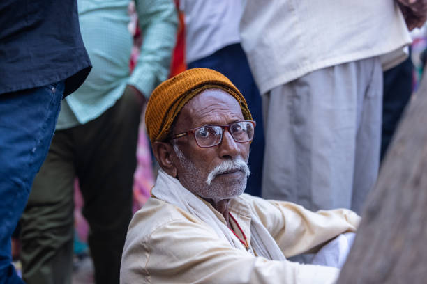 Ghaziabad, Uttar Pradesh, India - November 2023: Portrait of an old male sitting towards bank of river hindon to perform chhath puja with his family.