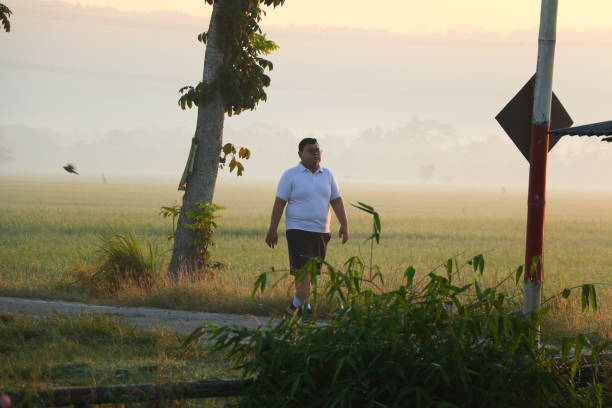 Cilacap, Indonesia - June 18, 2024 : A young, fat man walking after jogging on a sunny morning