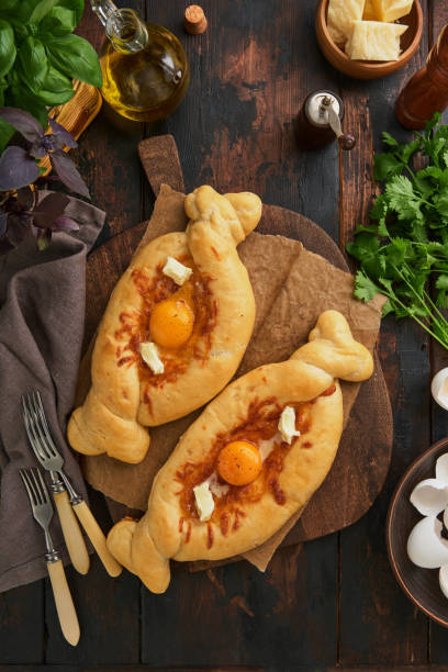 istock Khachapuri pie in Ajarian. Open pie with cheese and egg on wooden board with ingredients, basil, cilantro, egg yolk and spices. Traditional Georgian cuisine. Top view. Copy Space. 2162677654
