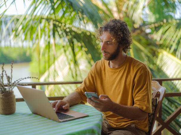 Man working with laptop and smartphone sitting on the patio under the palm trees Man working with laptop and smartphone sitting on the patio under the palm trees during his workation in Sri Lanka sri lanka business stock pictures, royalty-free photos & images