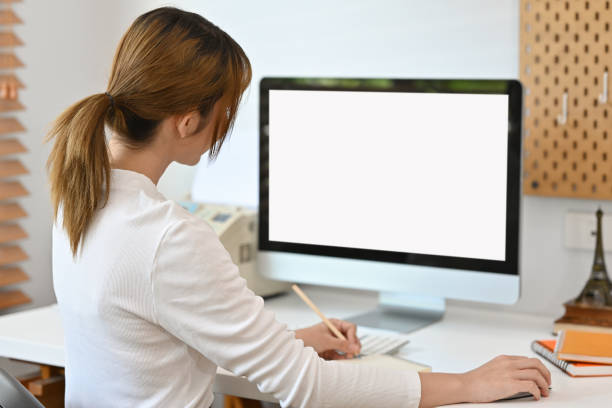 istock Rear view with female office worker using computer at her desk, Empty of device screen. 2162681489