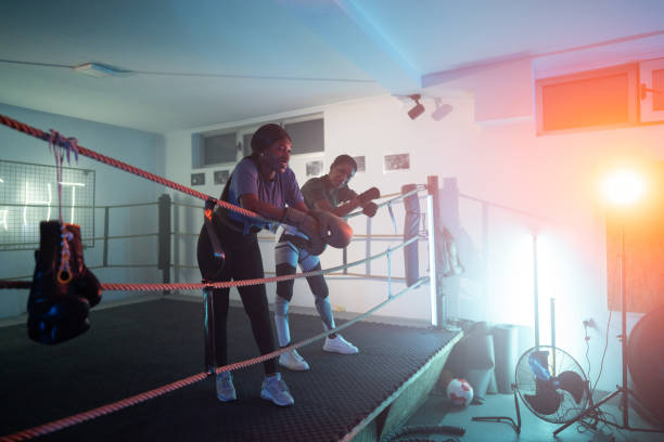 Two young African women leaning on ropes in boxing ring and resting after training