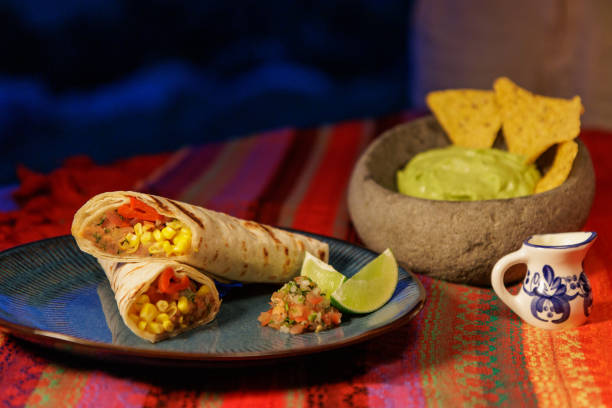 istock burritos with various fresh ingredients pico de gallo and lime on a blue design plate accompanied by a stone bowl with guacamole and tortilla chips and a porcelain sauce server on a handmade tablecloth with traditional colors in a blue atmosphere. 2162685684
