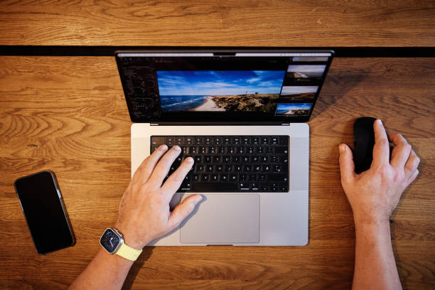 Cropped hands of man working over laptop with mouse and mobile phone on wooden desk in office
